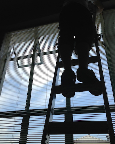 man installing aluminium blinds up a ladder