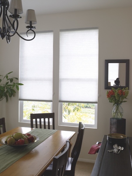 Light-filtering honeycomb blinds in white fabric installed in a dining room, allowing natural light while providing privacy.