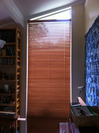 Wooden venetian blind fitted below an angled window with the shaped glass left uncovered