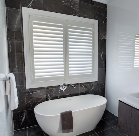 White plantation shutters in a bathroom beside a freestanding bathtub